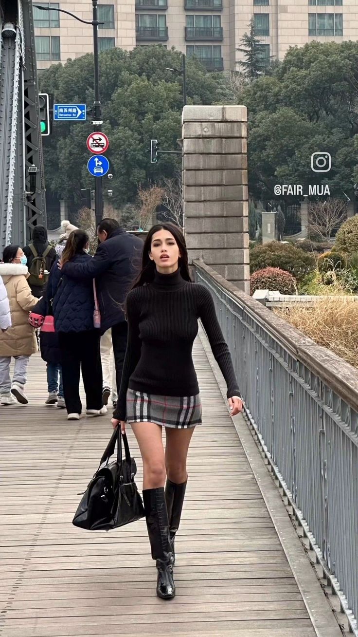 Woman in a black turtleneck and plaid skirt walking on a bridge
