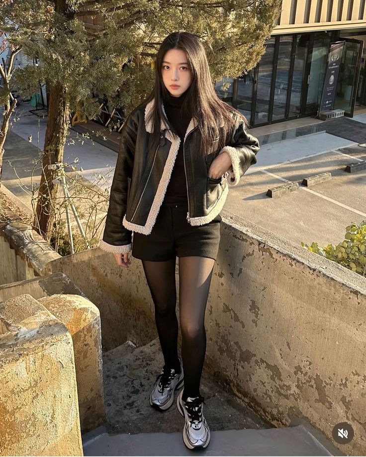 Woman in a black jacket and shorts with tights standing on outdoor stairs