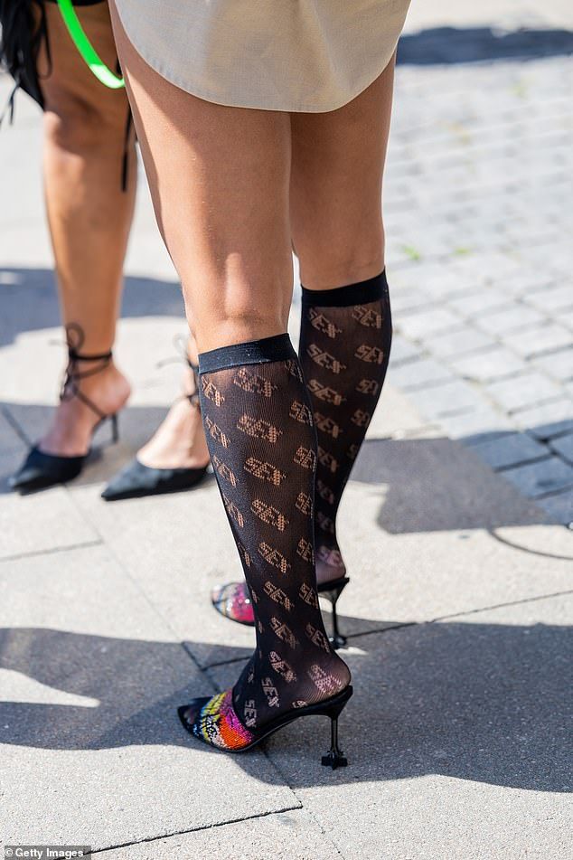 Legs of two people, one wearing sheer socks with 'SEX' pattern and high heels