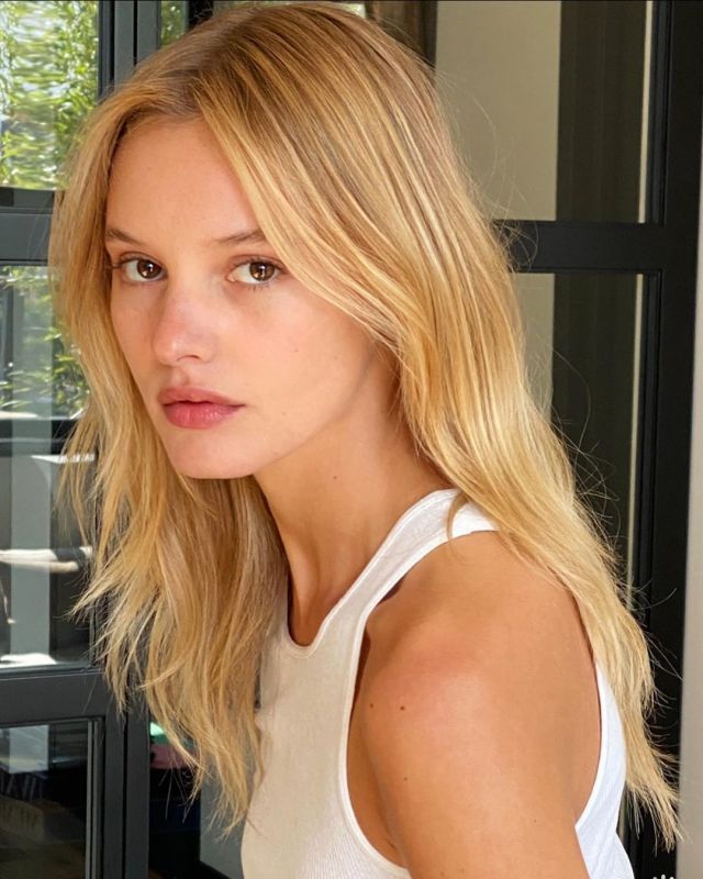 Woman with long blonde hair wearing a white tank top, looking at the camera