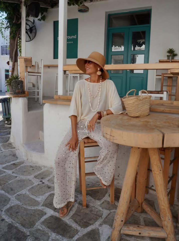 Woman in a wide-brim hat and sequin pants sitting at an outdoor cafe