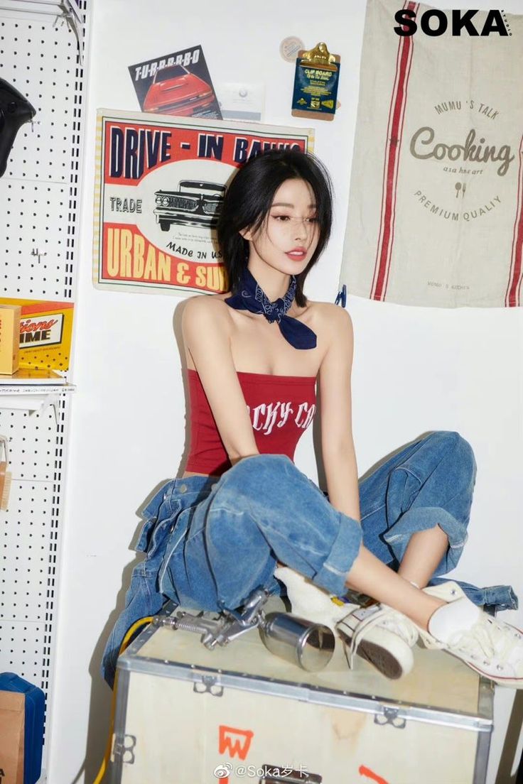 Woman with short black hair wearing a red tube top and jeans, sitting indoors