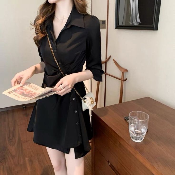 Woman in a black dress holding a newspaper indoors