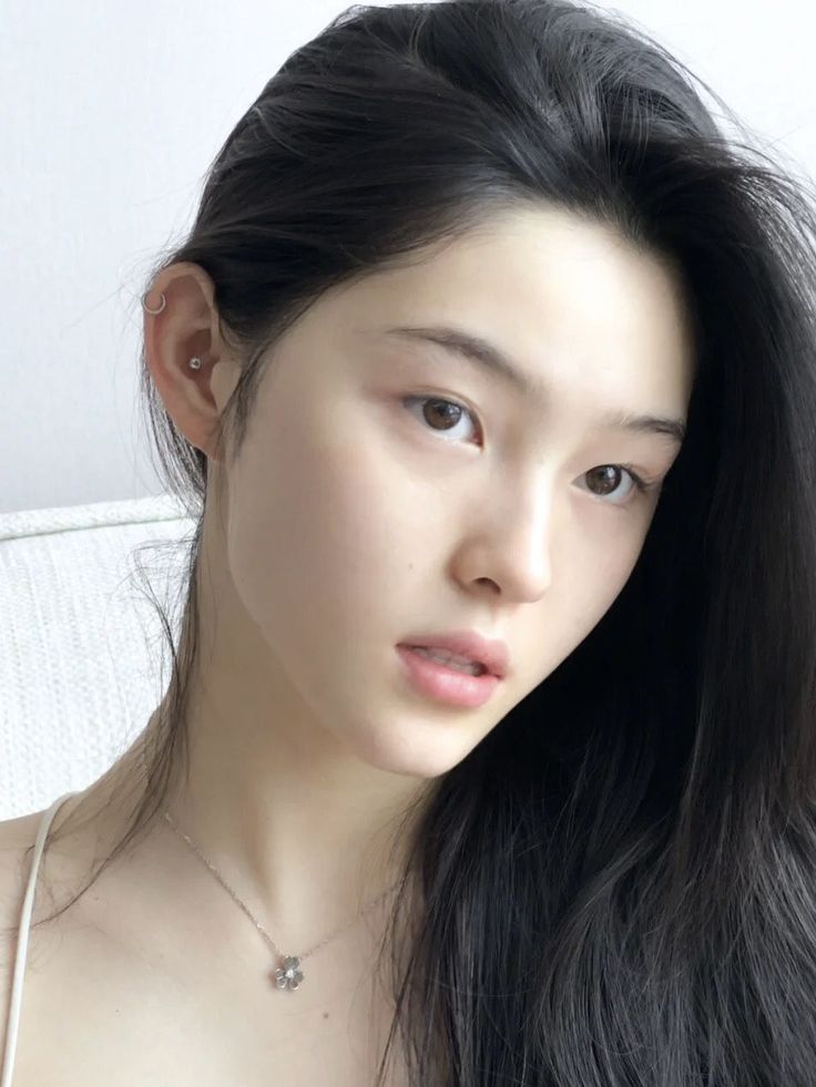 Woman with long black hair and a necklace, looking directly at the viewer