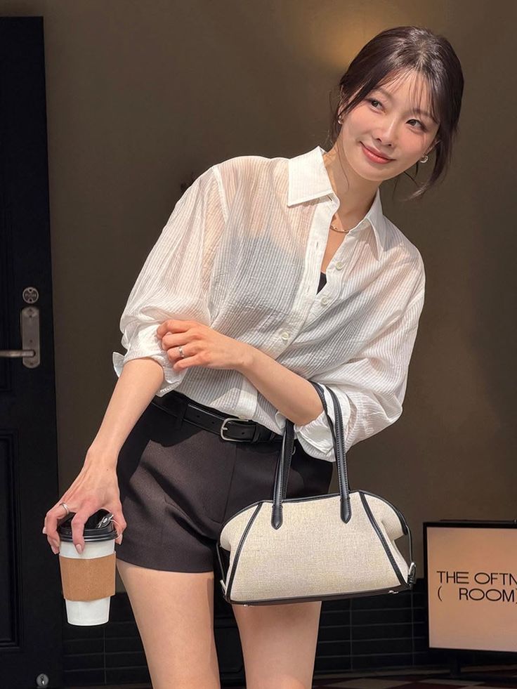 Woman in a white shirt and black shorts holding a coffee cup and bag