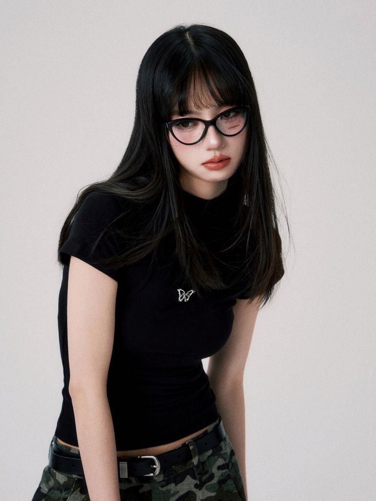 Woman with long black hair and glasses wearing a black t-shirt and camouflage skirt