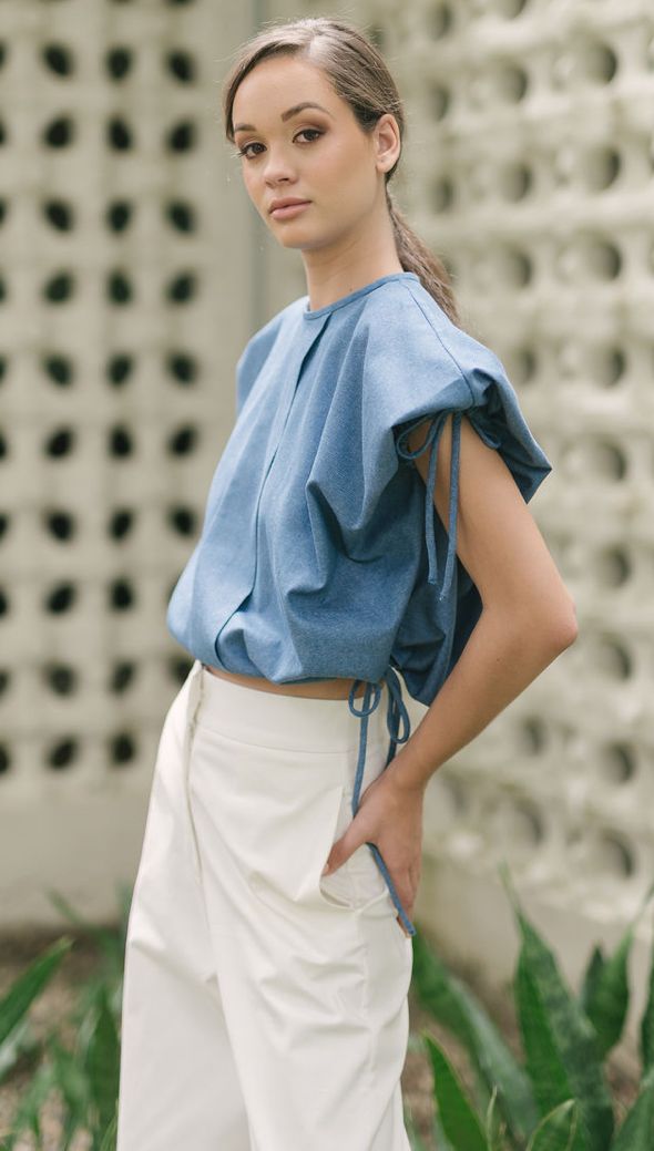 Woman in a blue top and white pants posing outdoors
