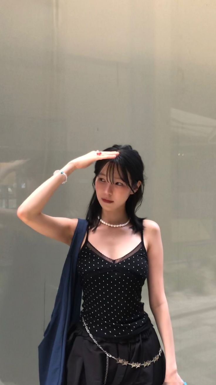 Woman in a black polka dot top and star chain belt, shielding her eyes