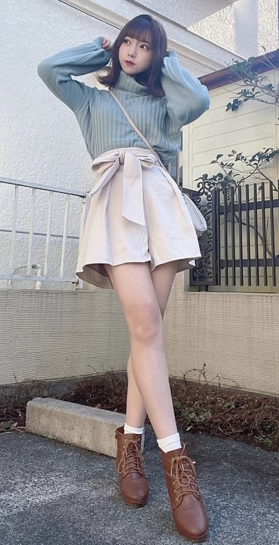 Woman in a light blue turtleneck and paperbag shorts posing outdoors