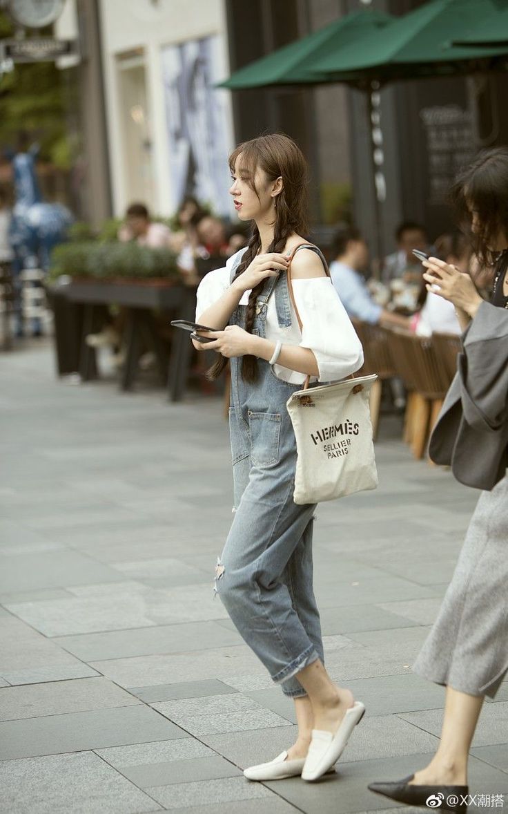 Woman in denim overalls and an off-shoulder top walking on a street