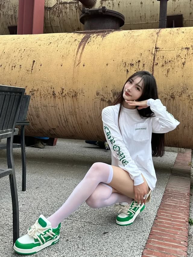 Woman in a white long-sleeve shirt and white thigh-highs squatting outdoors