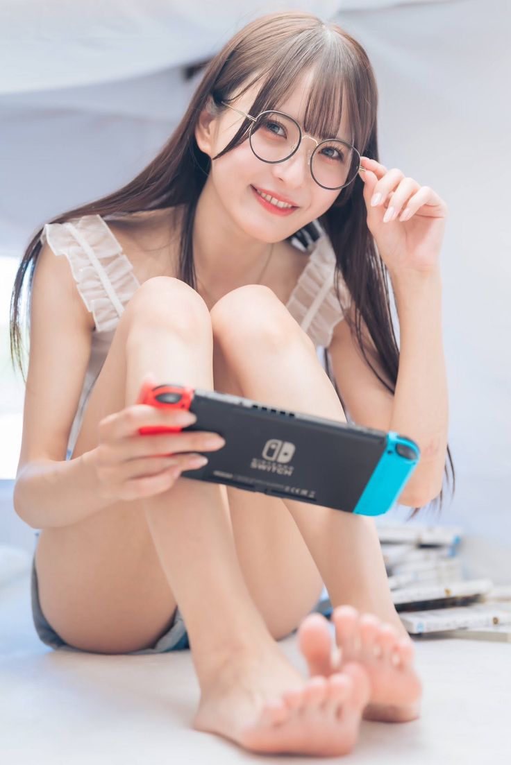 Woman with long hair and glasses holding a Nintendo Switch while sitting indoors
