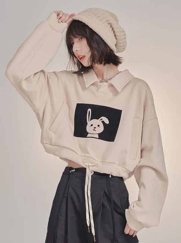 Woman with short hair and a beanie wearing a cropped sweatshirt with a bunny print