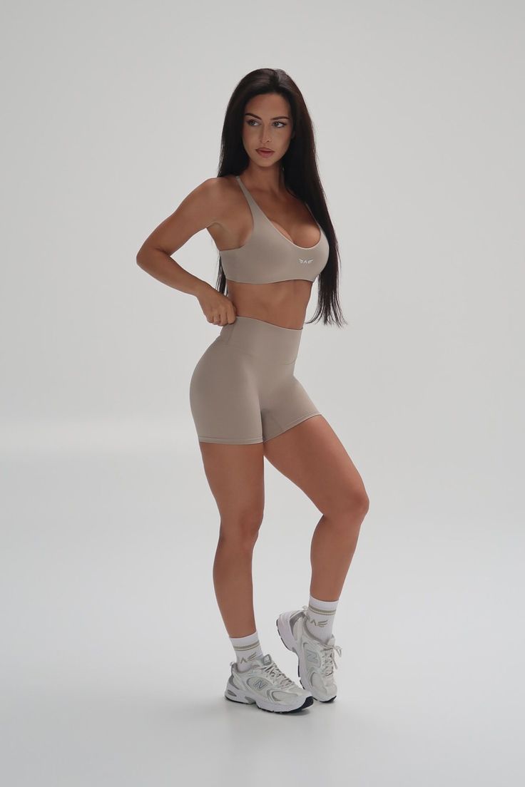 Woman in a beige sports bra and athletic shorts posing in a studio