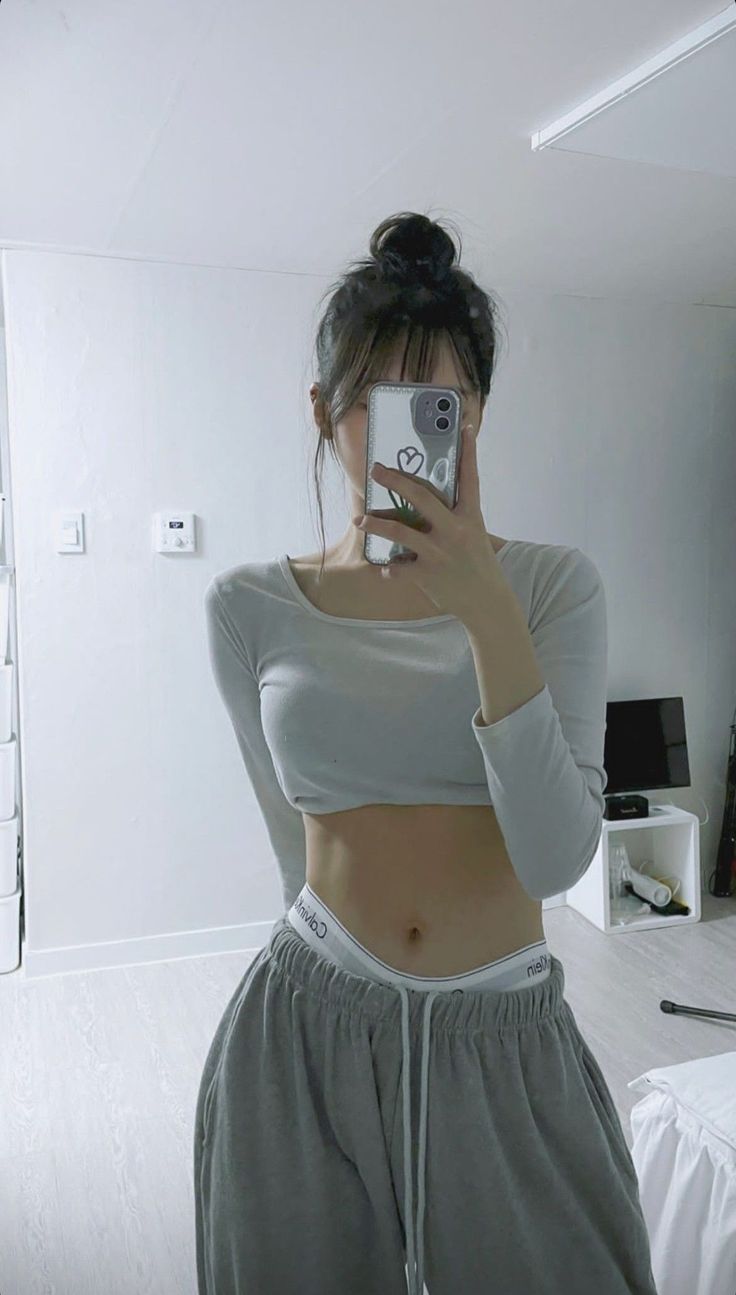 Woman in a crop top and sweatpants taking a mirror selfie