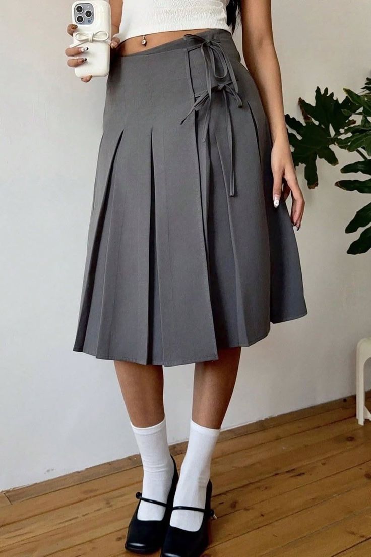 Person in a gray pleated skirt and white crop top holding a phone