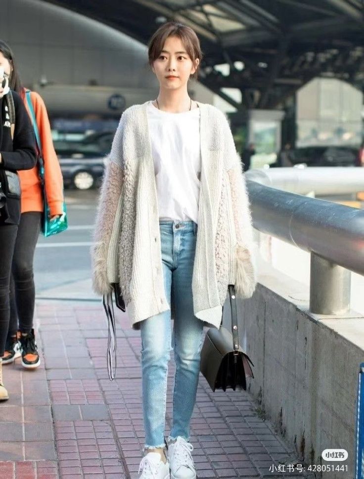 Woman in a white cardigan, jeans, and sneakers walking outdoors
