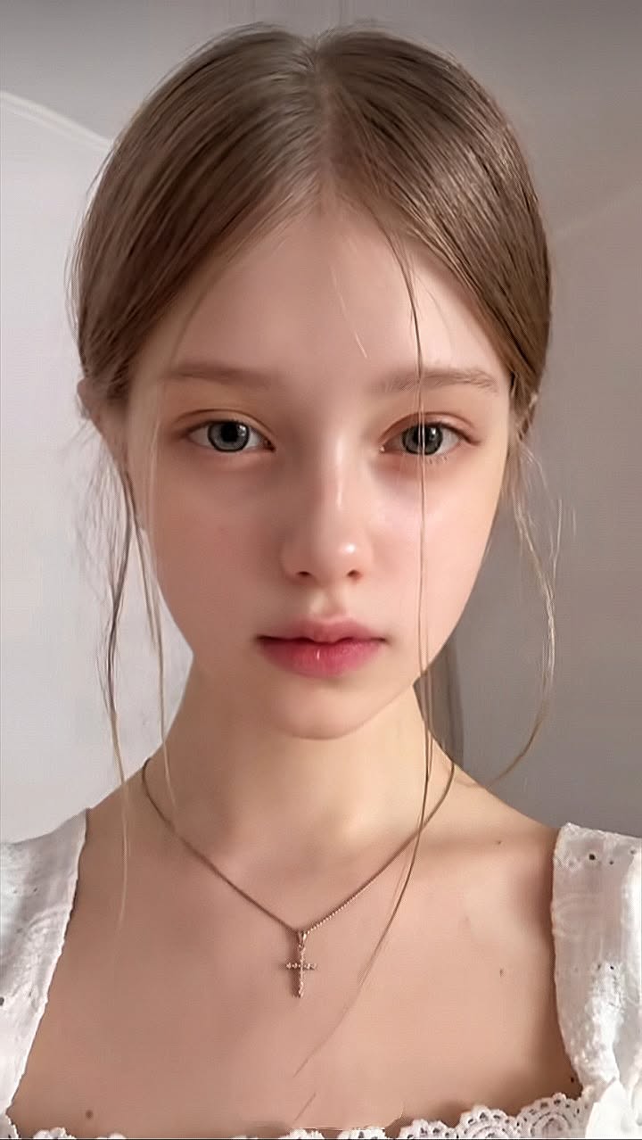 Young woman with long hair and a cross necklace looking directly at the viewer