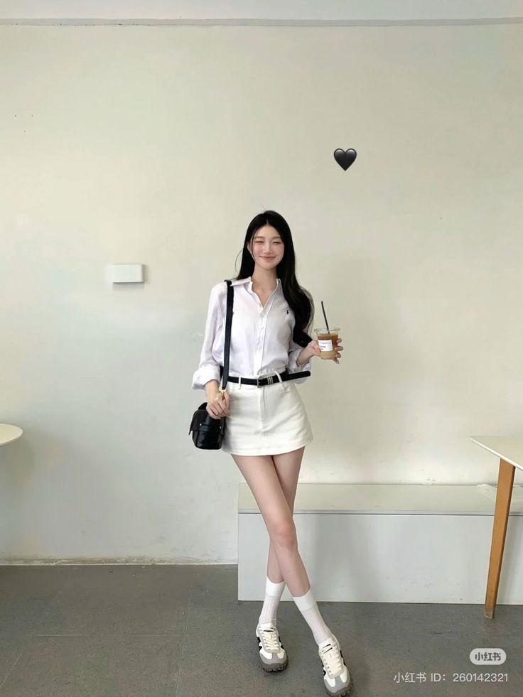 Woman in a white shirt and skirt holding a drink indoors