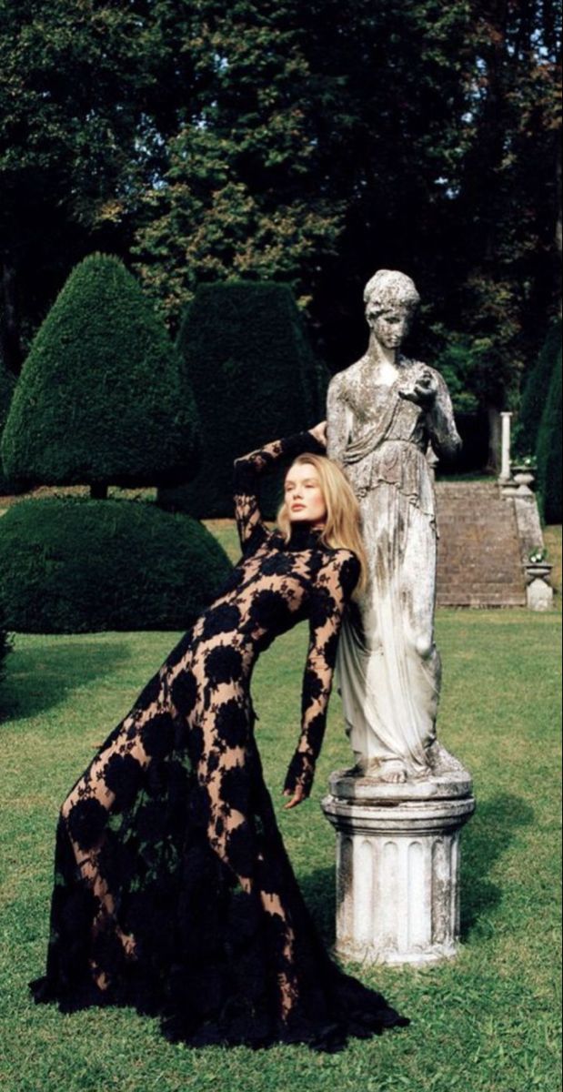Woman in a black lace dress posing next to a statue in a garden