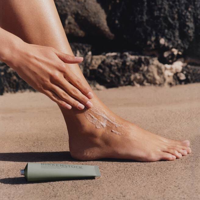 Person applying lotion to their foot outdoors