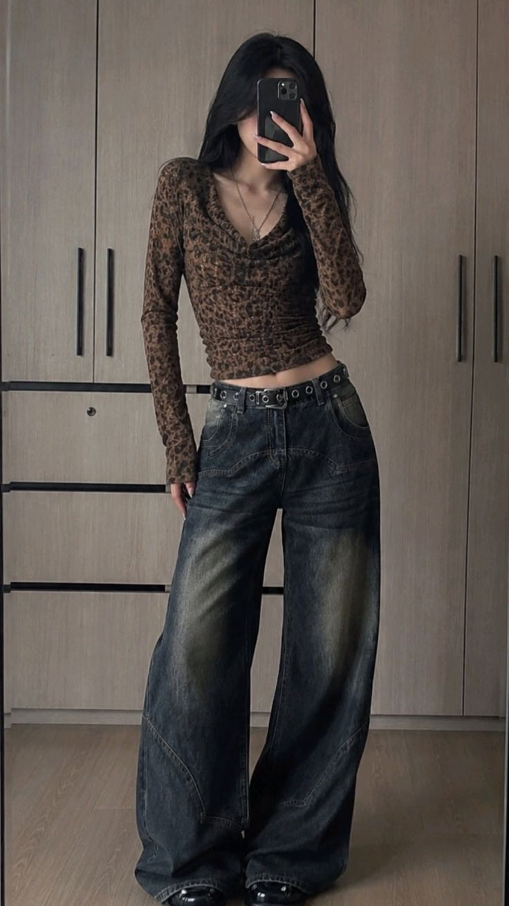 Person in a leopard print top and baggy jeans taking a mirror selfie indoors