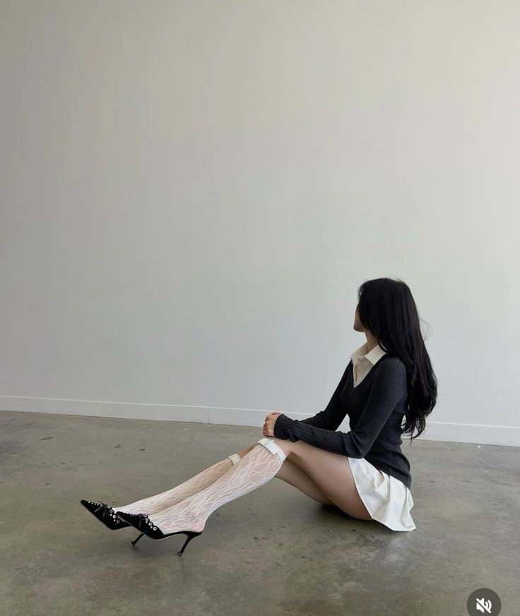 Woman with long black hair sitting on the floor in a white mini skirt and lace socks
