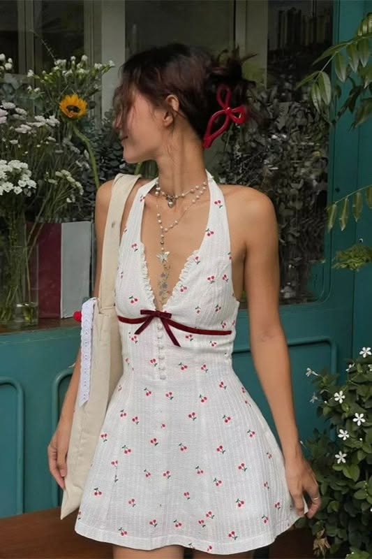 Woman in a white cherry print halter dress with a red hair clip outdoors