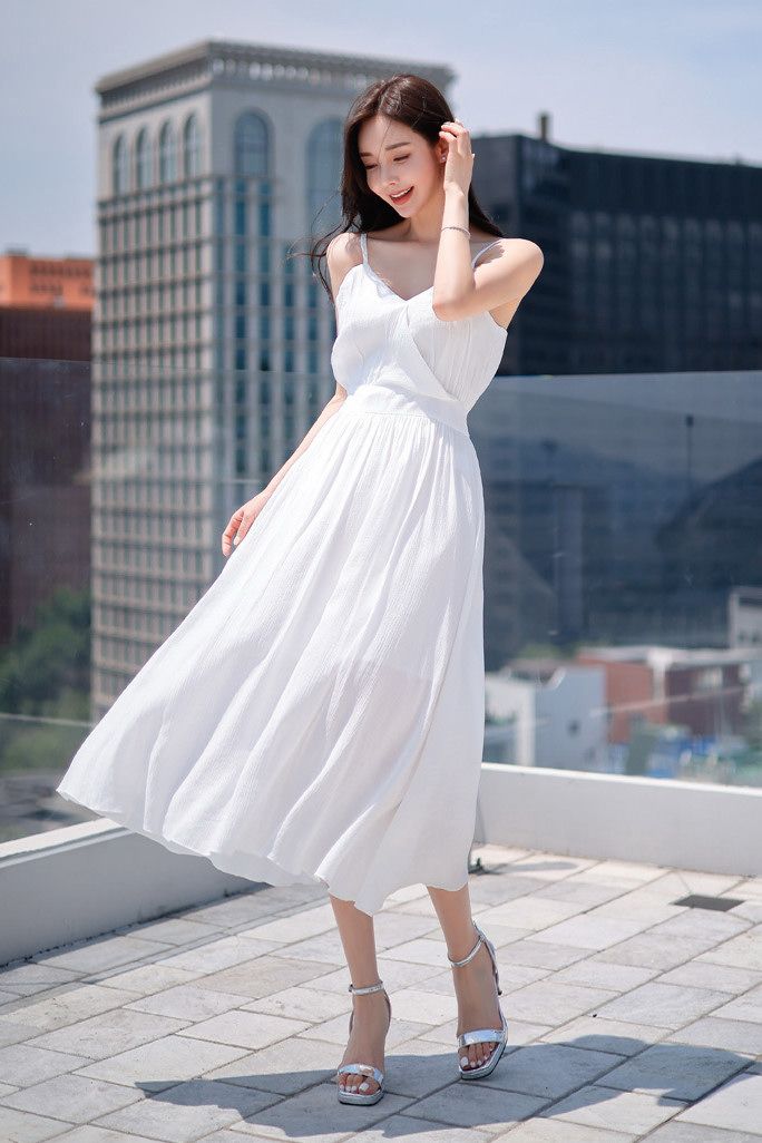 Woman in a white dress and silver heels on a rooftop with a cityscape background