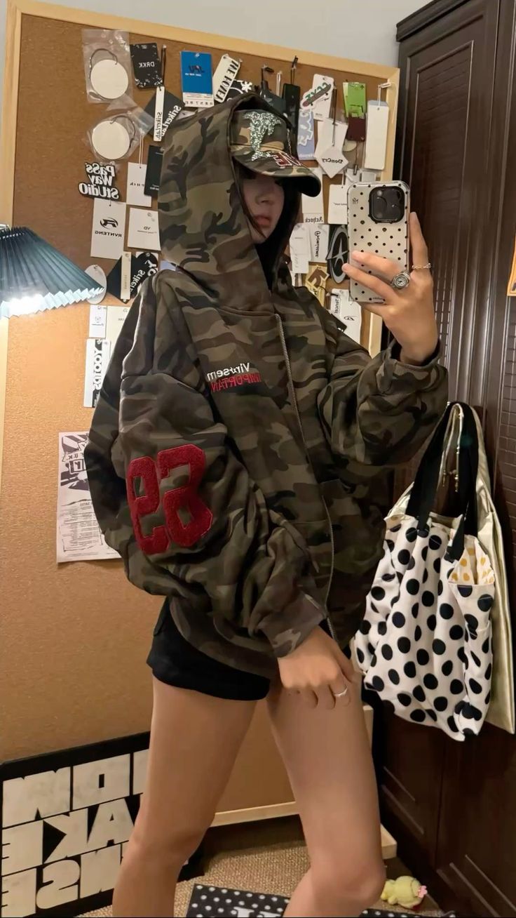 Person in a camouflage hoodie and baseball cap taking a mirror selfie