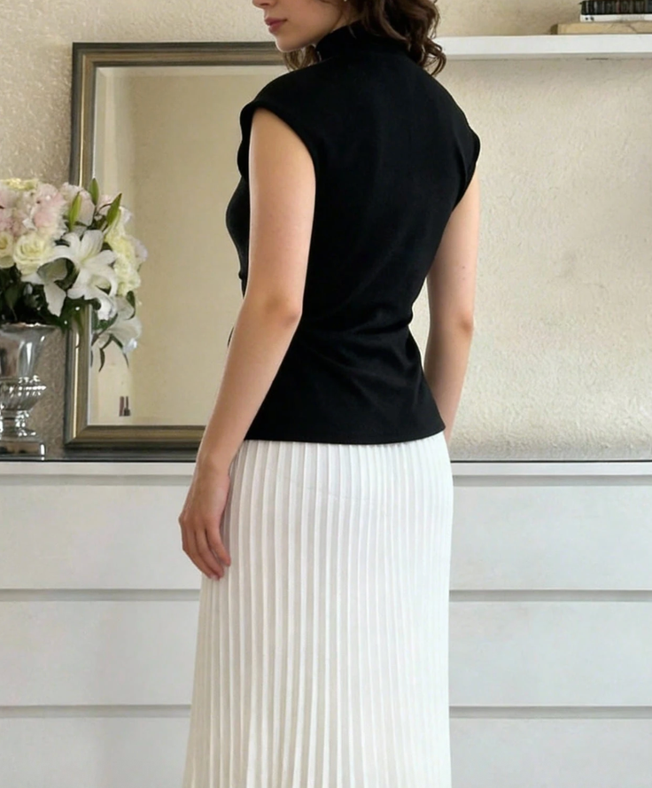 Woman in a black top and white pleated skirt, seen from behind indoors