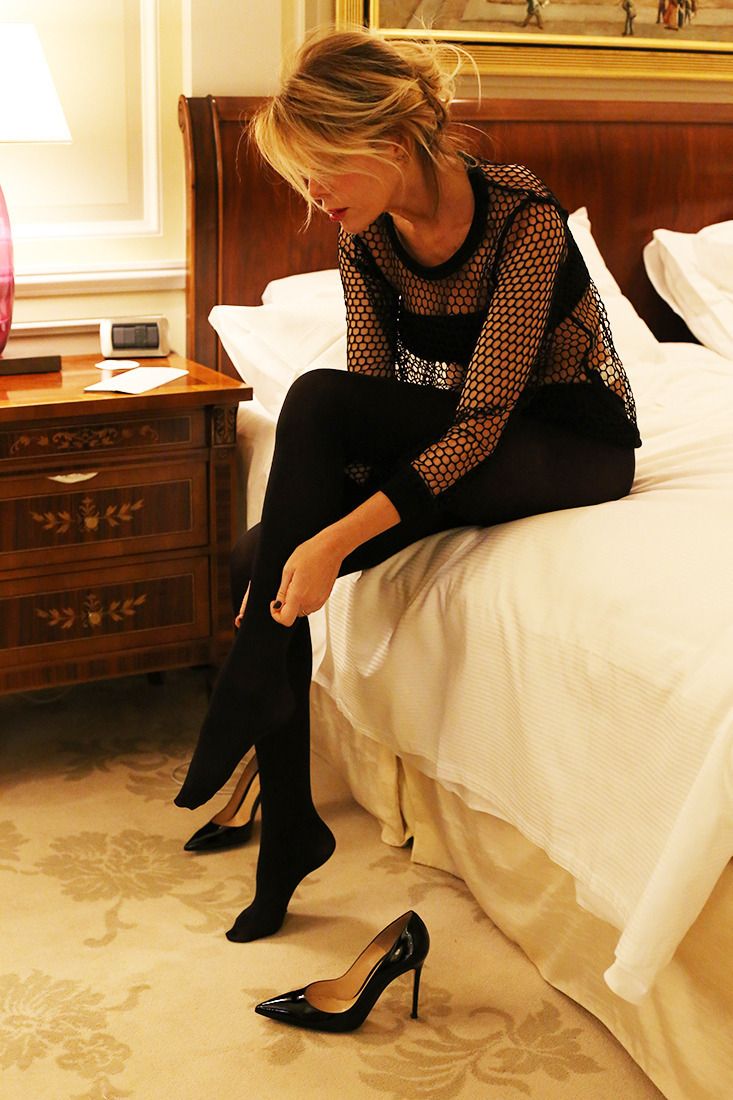 Woman in a fishnet top and black tights sitting on a bed