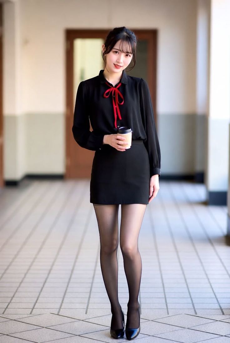 Woman in a black blouse and mini skirt holding a cup indoors