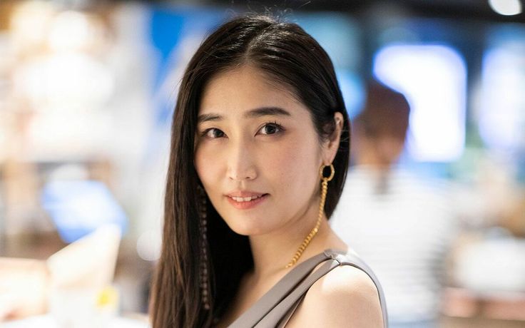 Woman with long dark hair and gold earrings in a gray top