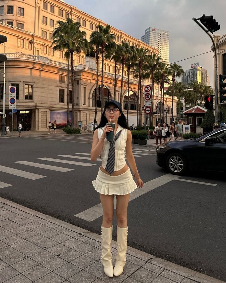Woman in a white pleated skirt and crop top on a city street with palm trees