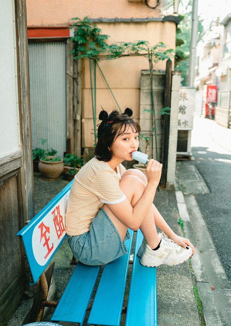 Woman with space buns eating a popsicle on a blue bench outdoors