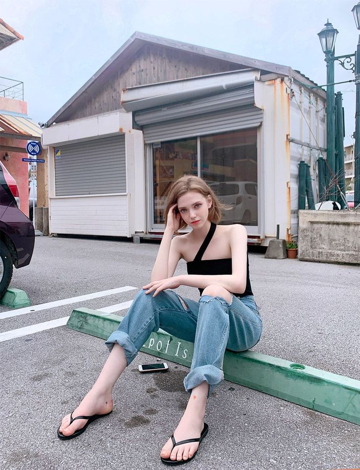 Woman in a black top and ripped jeans sitting on a street curb