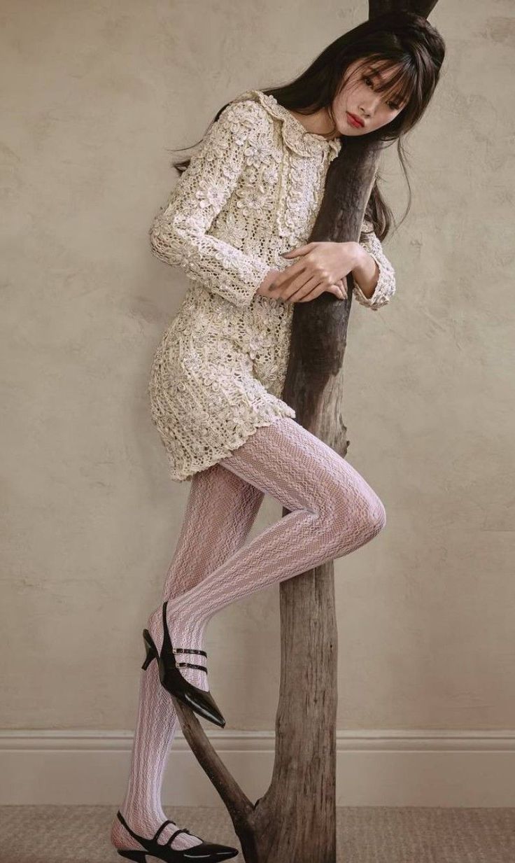 Woman in a crochet dress and patterned tights leaning on a wooden post