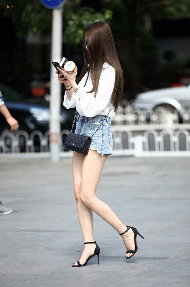 Woman with long hair wearing denim shorts and a white shirt walking outdoors