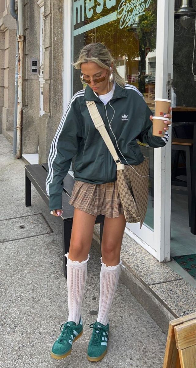 Woman in a plaid skirt and adidas jacket holding coffee on a street