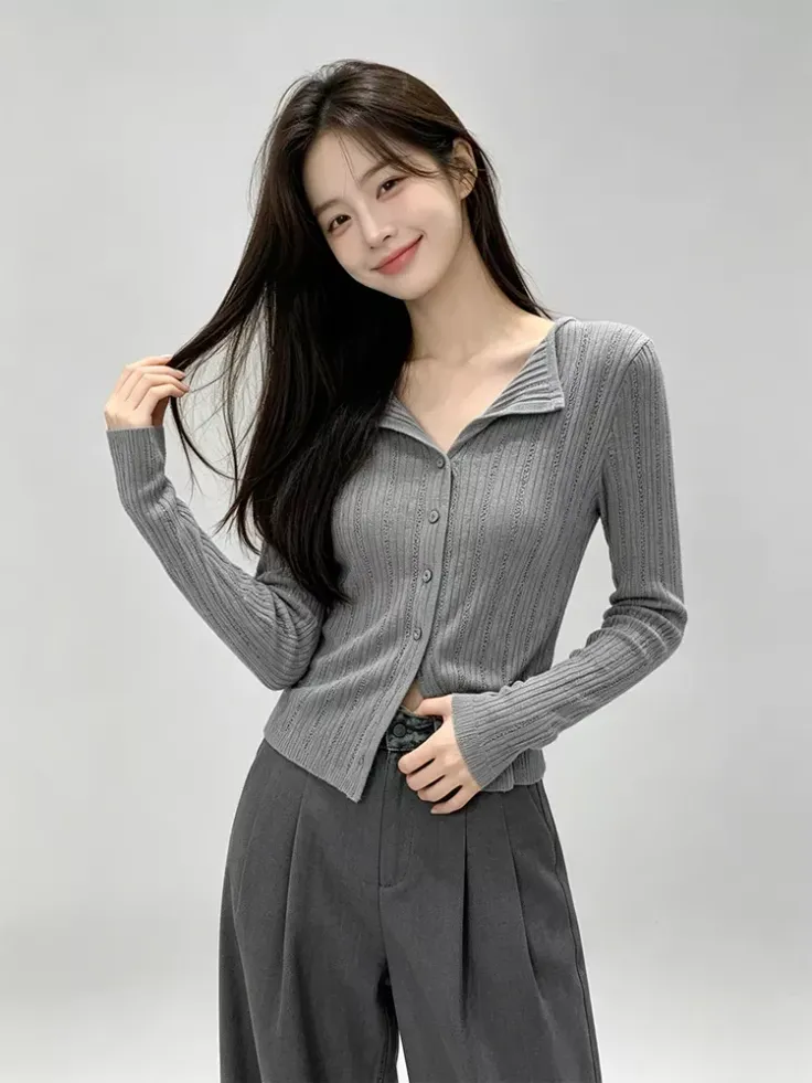 Woman with long dark hair wearing a gray collared cardigan and dark pants