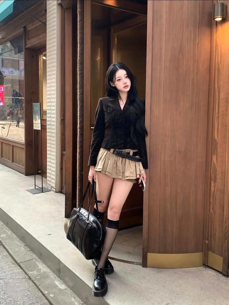 Woman with long black hair in a mini skirt and black jacket holding a handbag