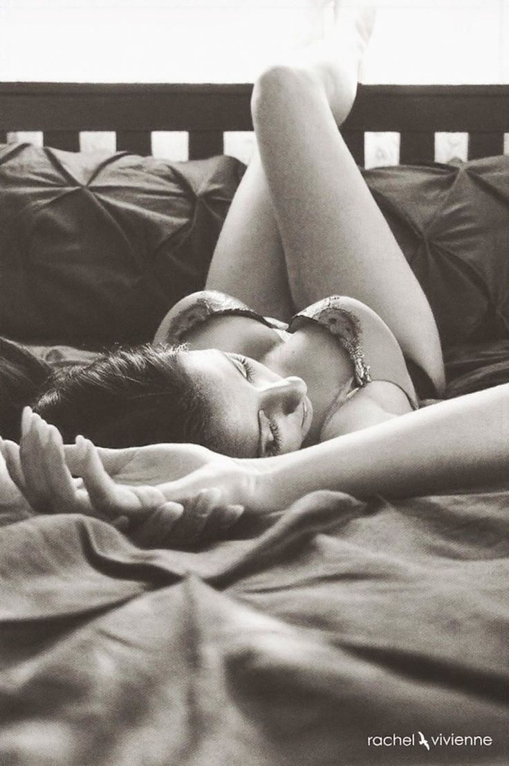 Woman in lingerie lying on a bed with legs raised, in black and white