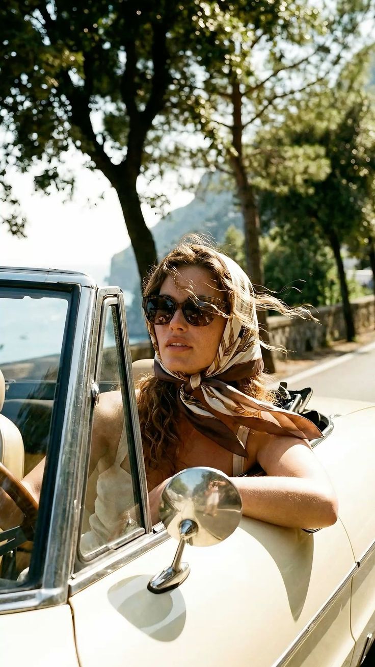 Woman in a head scarf and sunglasses driving a convertible car