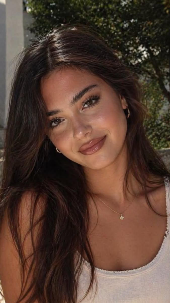 Woman with long brown hair and hoop earrings smiling outdoors
