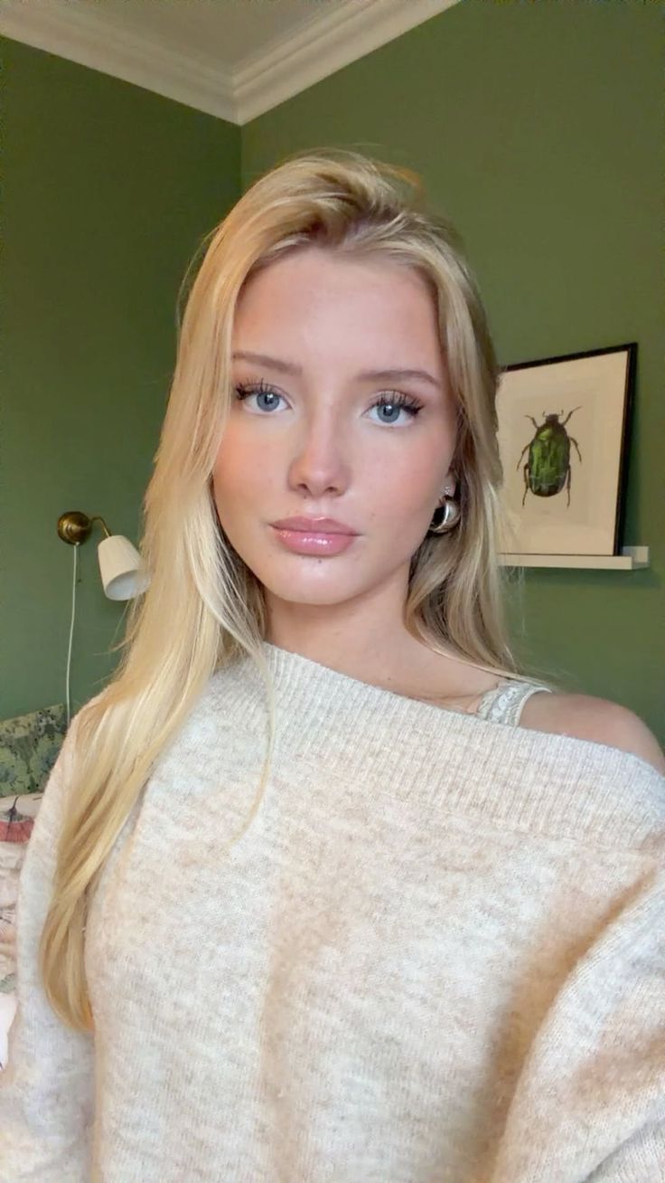 Blonde woman in an off-shoulder sweater with a green wall background