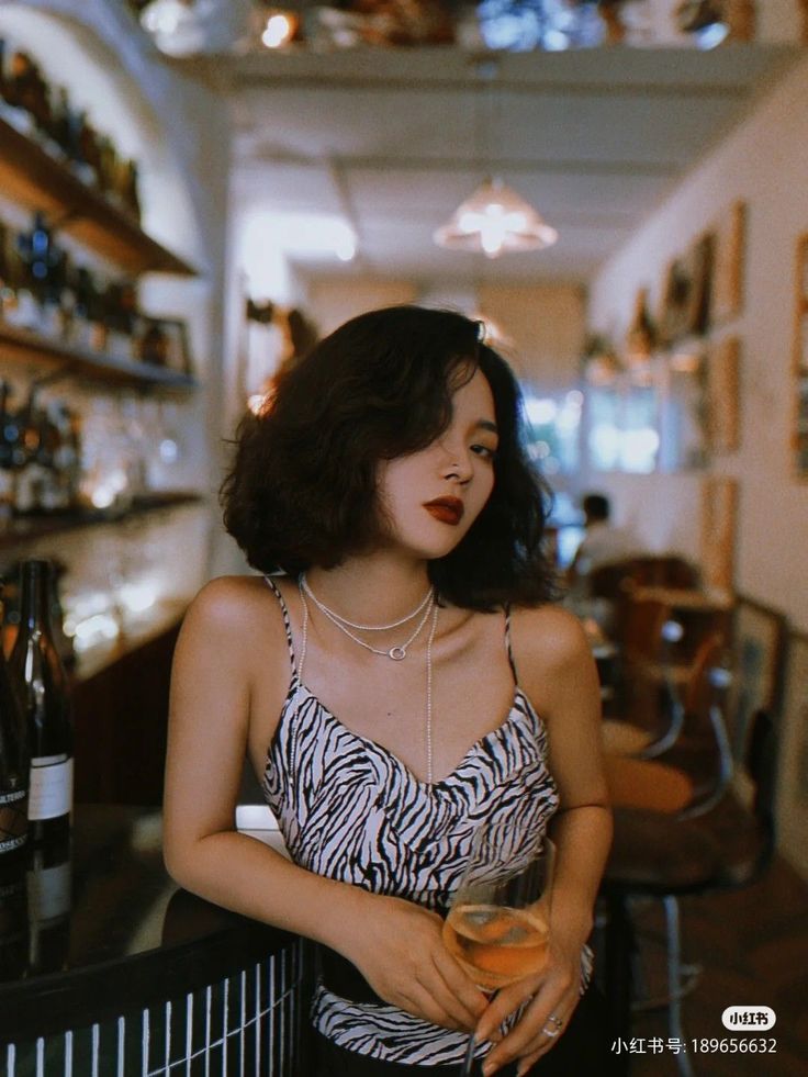 Woman with short hair and red lipstick holding a wine glass at a bar