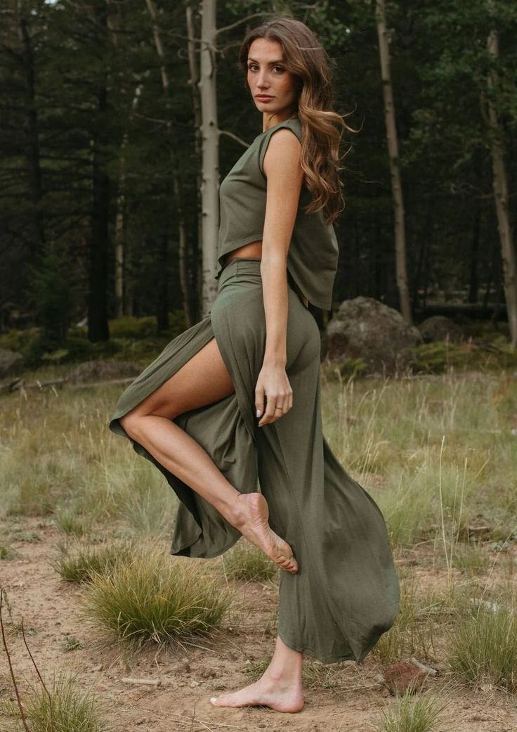 Woman in an olive green outfit with a high slit in a forest setting