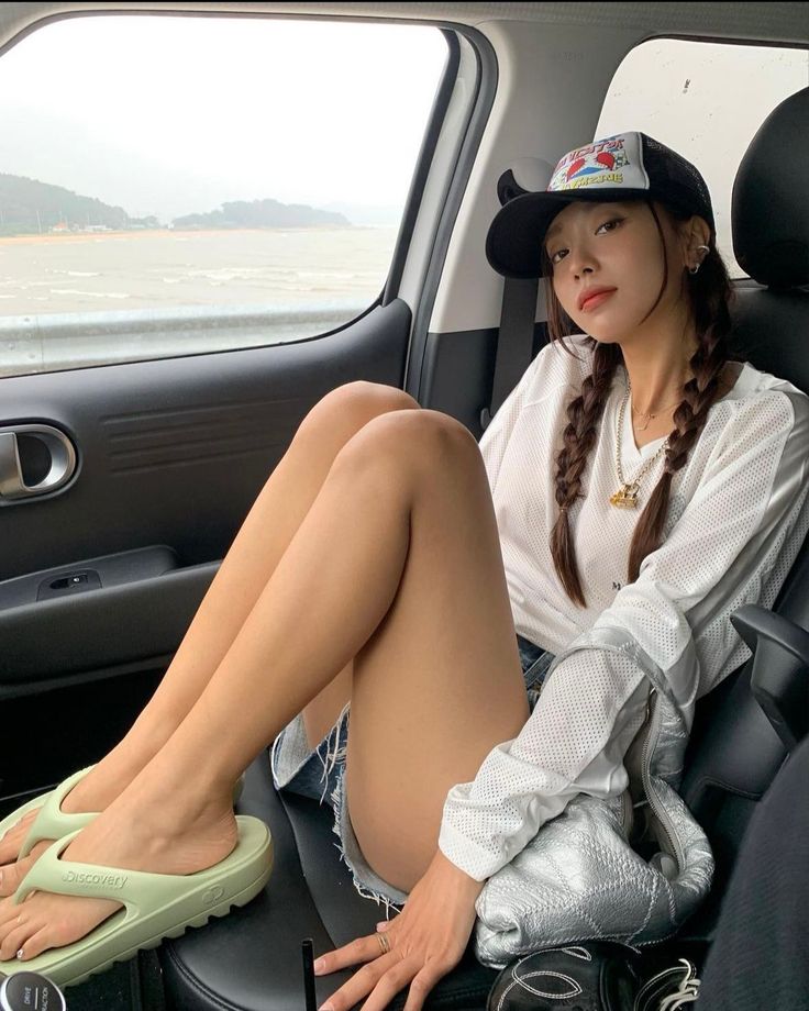 Woman with braids and a baseball cap sitting in a car with a beach view