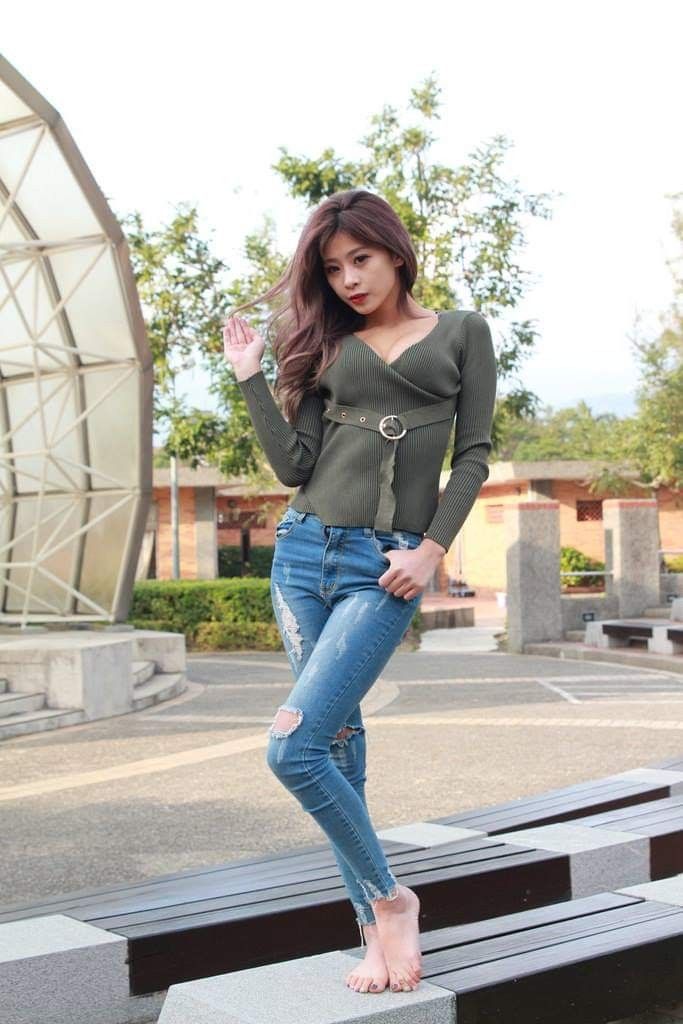 Woman in a green v-neck top and ripped jeans posing outdoors